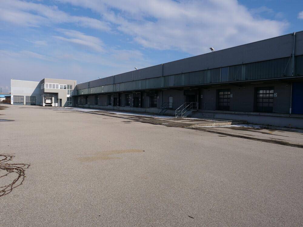 Lange Fassade eines Industriegebäudes mit mehreren Laderampen und einem weitläufigen asphaltierten Vorplatz.