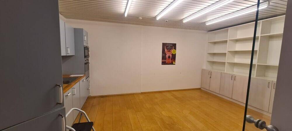Heller Büroraum mit Küchenzeile, weißen Regalen und Holzdecke, ideal für Arbeitsbereiche.