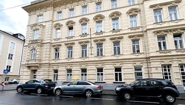 Klassisches Mehrfamilienhaus mit reich verzierter Fassade und parkenden Autos auf der Straße.