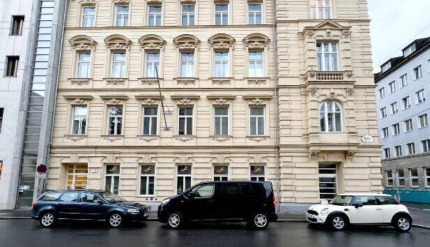 Historisches Gebäude mit klassischer Architektur, vielen Fenstern und parkenden Autos auf der Straße.