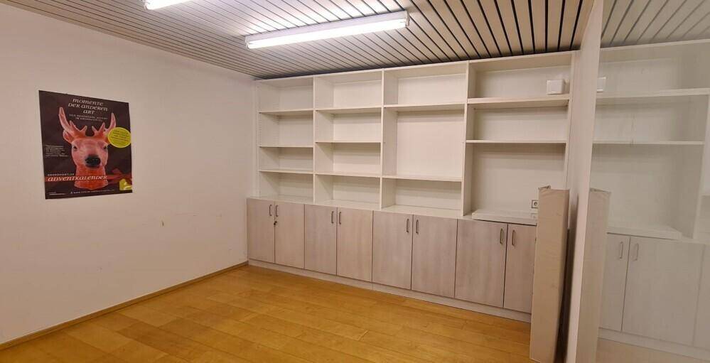 Geräumiger Büroraum mit weißen Regalen, Holzboden und einer modernen Deckenbeleuchtung.