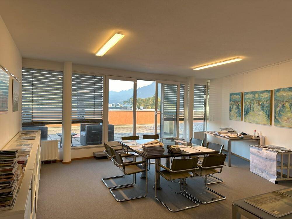 Geräumiger Büroraum mit großem Besprechungstisch und Zugang zur Terrasse, mit Blick auf die Berge.