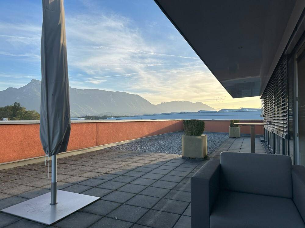 Geräumige Dachterrasse mit Sonnenschirm und Sitzgelegenheiten, die einen weiten Blick auf die umliegenden Berge bietet.