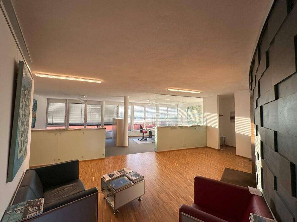 Offener Bürobereich mit Holzboden, Loungebereich und modernen Glasabtrennungen für Arbeitsplätze.