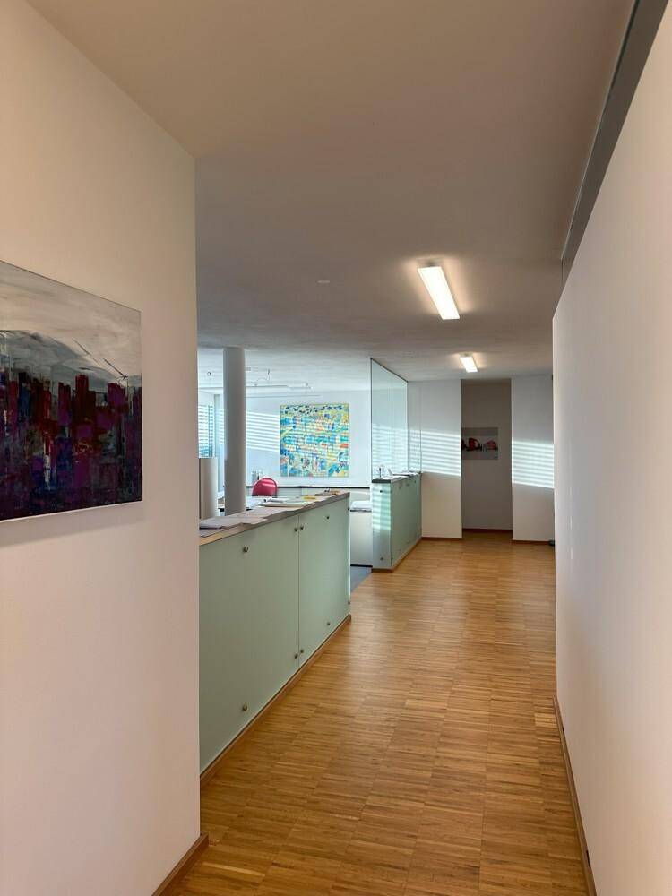 Heller Flur mit Holzboden und modernen Glasabtrennungen, der zu weiteren Bürobereichen führt.