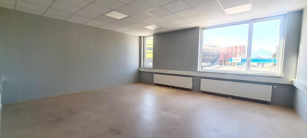 Heller Büroraum mit großen Fenstern, die viel Tageslicht hereinlassen, und Heizkörpern unter den Fensterbänken.