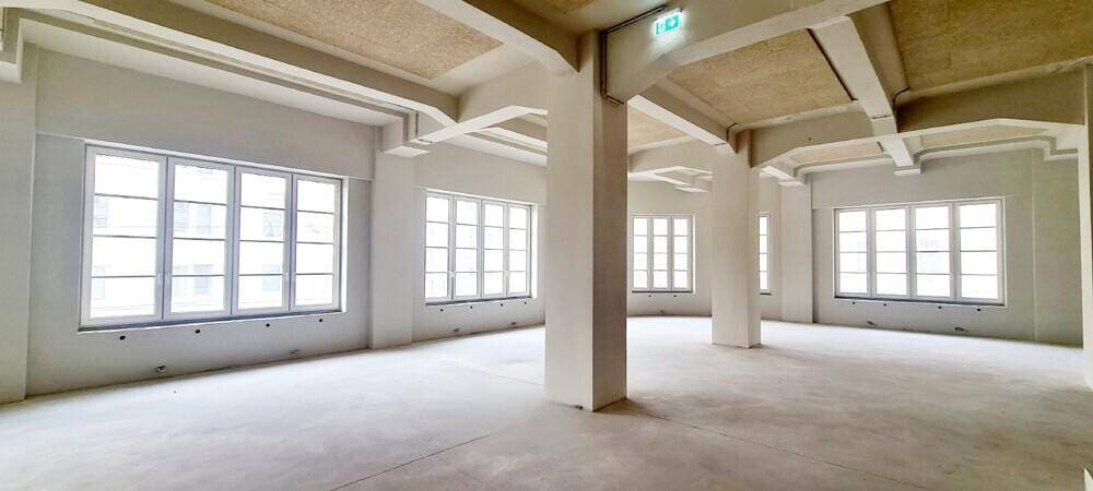 Großzügiger, heller Büroraum mit vielen Fenstern und hohen Decken, der eine offene und flexible Gestaltung ermöglicht.