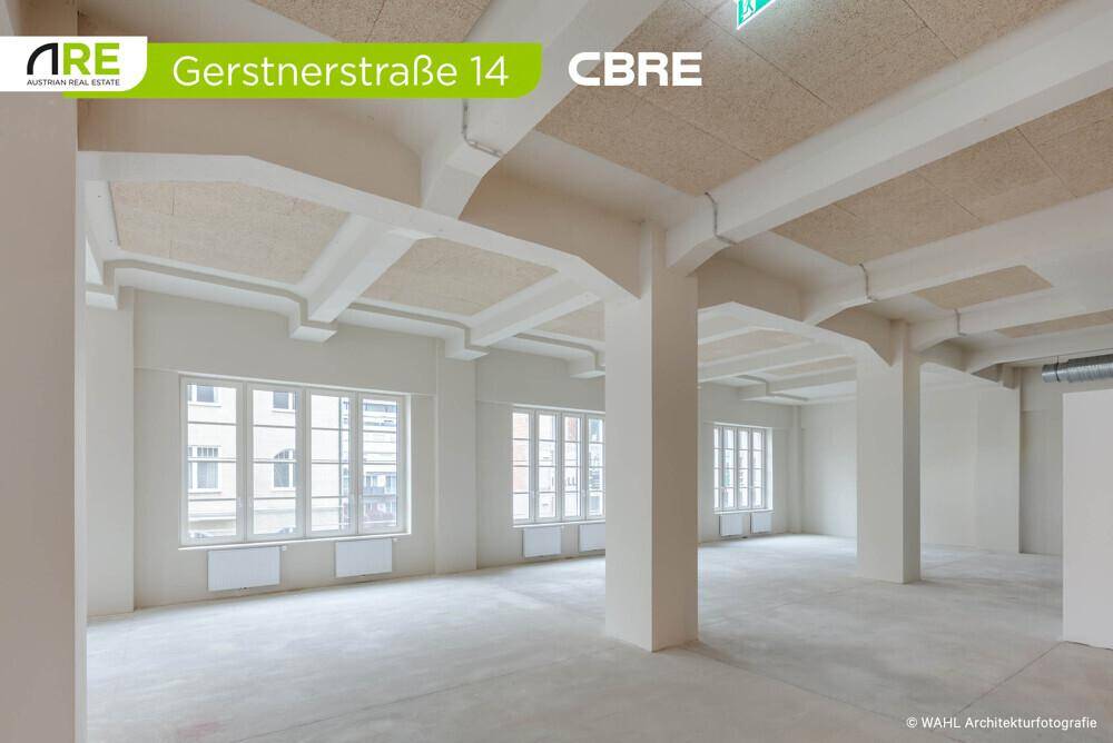 Heller Bürobereich mit großen Fenstern, hohen Decken und Betonboden, ideal für eine moderne Arbeitsumgebung.