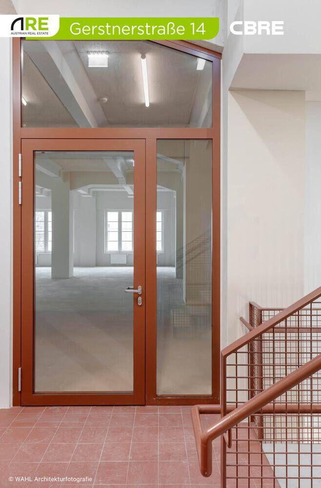 Eingangsbereich mit einer großen Glastür und braunem Rahmen, die in den Bürobereich führt, neben dem Treppenhaus.