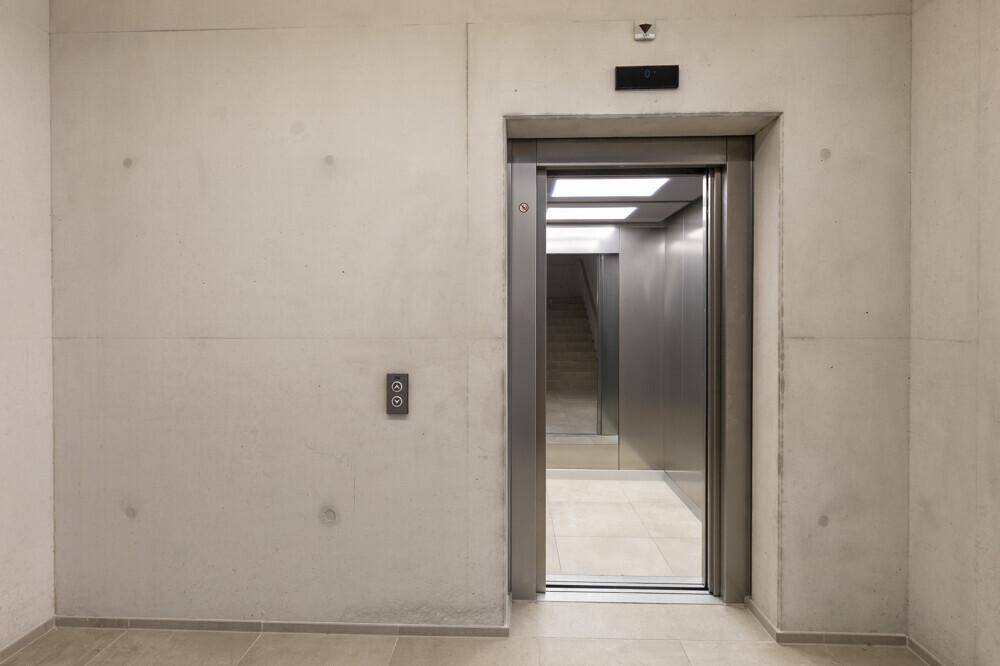 Moderner Aufzug in einem Gebäude mit Sichtbetonwänden und Fliesenboden.