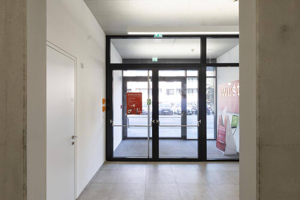 Heller Eingangsbereich mit großen Glastüren, Fliesenboden und modernen Leuchten.