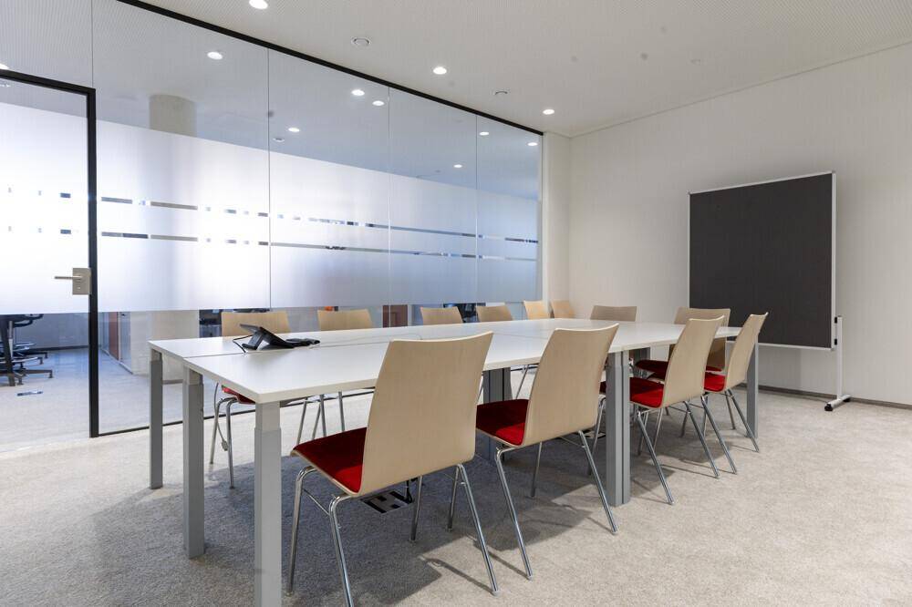 Heller Konferenzraum mit großem Tisch, beigen Stühlen und einer Glaswand.