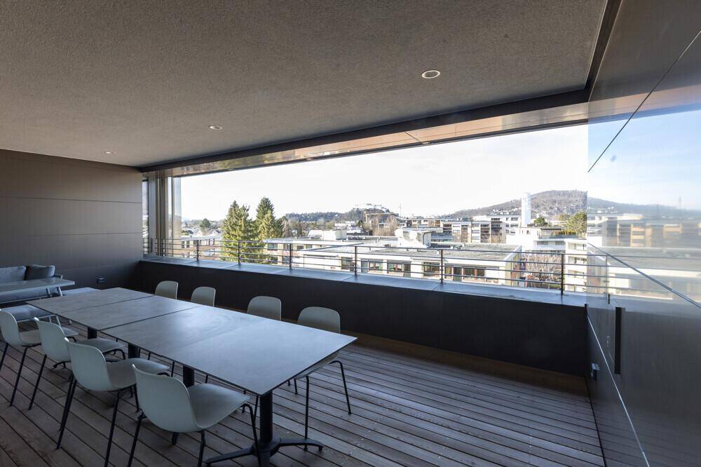 Großer Balkon mit Holzboden, Esstisch und weitem Blick über die Stadt und die umliegenden Hügel.