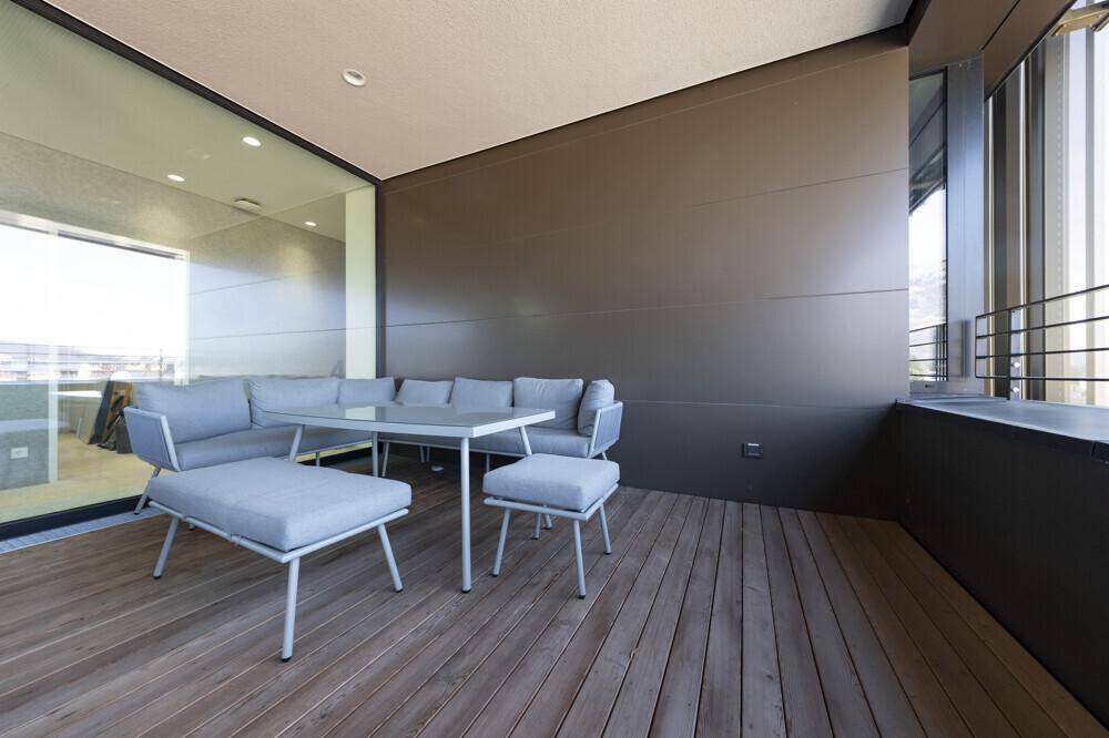 Geräumiger Balkon mit Holzboden und modernen Outdoor-Möbeln, ideal zum Entspannen im Freien.