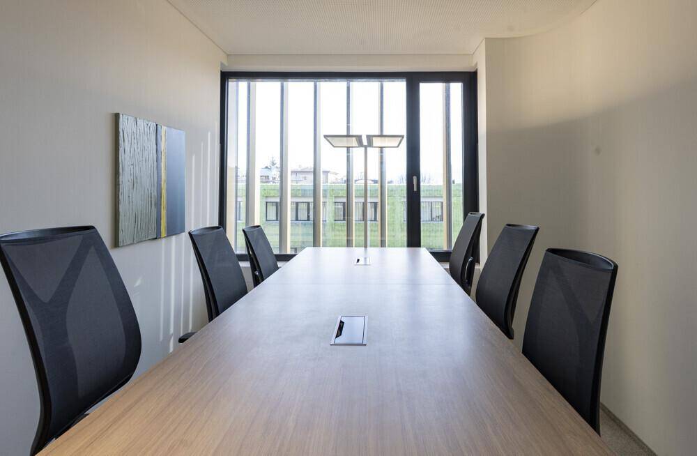 Moderner Konferenzraum mit großem Holztisch, bequemen Stühlen und viel Tageslicht durch die Fenster.