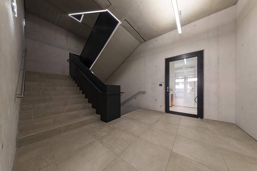 Modernes Treppenhaus mit Fliesenboden, schwarzem Geländer und indirekter Beleuchtung, die die Stufen hervorhebt.