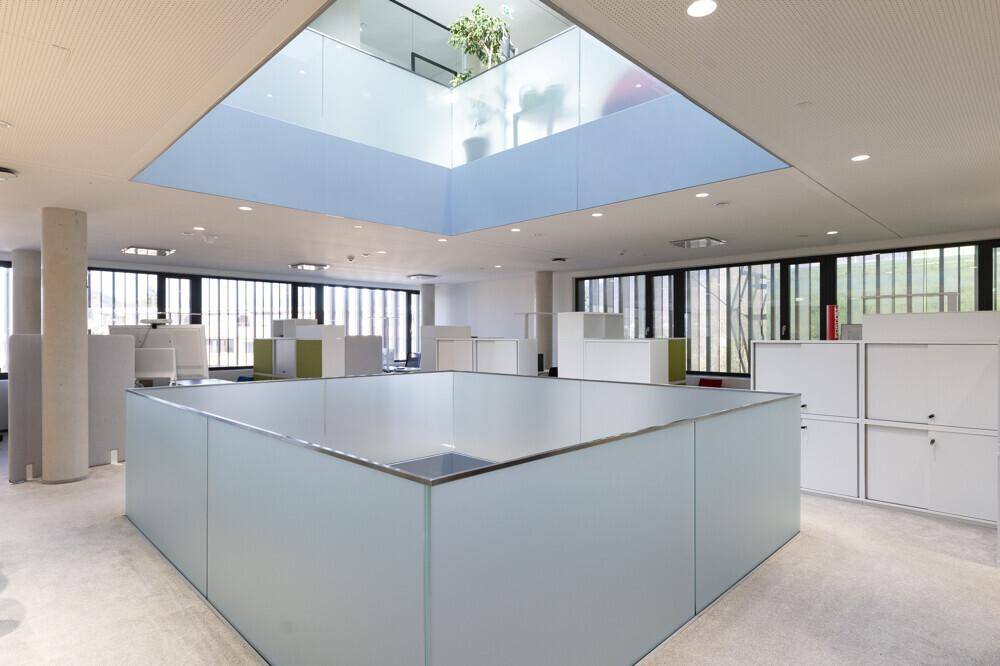 Offenes Büro mit einem zentralen Oberlicht und modernen Trennwänden, die eine helle Arbeitsumgebung schaffen.