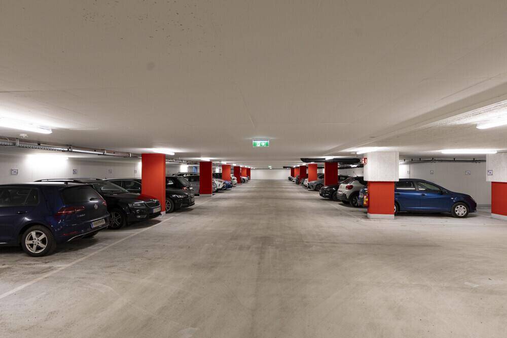 Geräumige Tiefgarage mit vielen Stellplätzen, hell beleuchtet und mit roten Säulen markiert.
