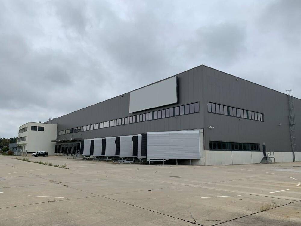 Weitläufiges Logistikgebäude mit großer Freifläche und Laderampen unter bewölktem Himmel.