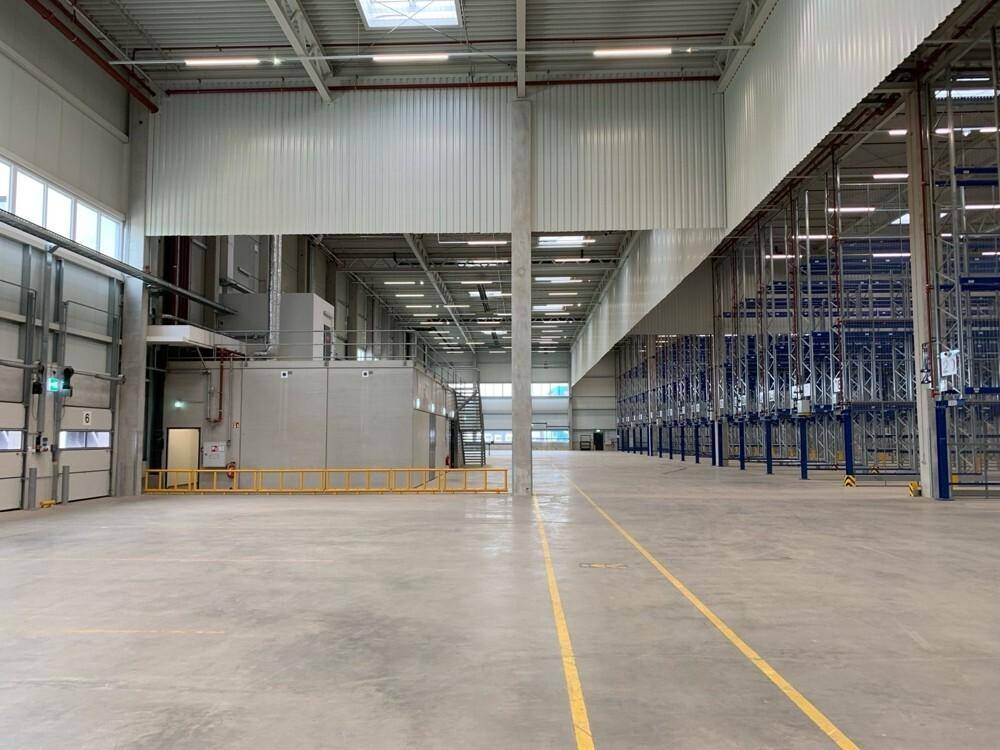 Große, helle Lagerhalle mit hohen Decken, Betonboden und internen Gebäudestrukturen.