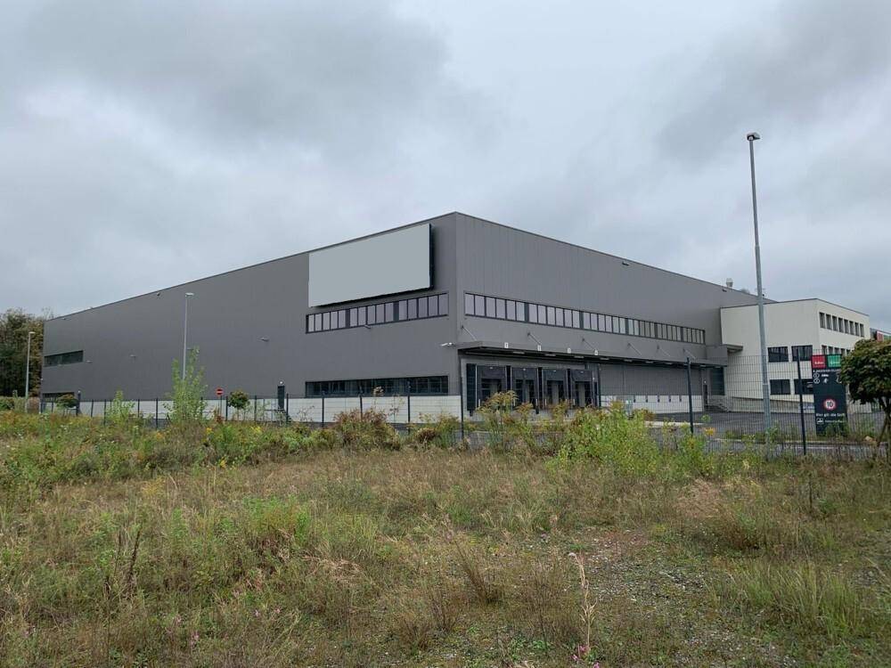 Ansicht des Logistikzentrums aus der Ferne mit umliegendem Grün und Parkplätzen.