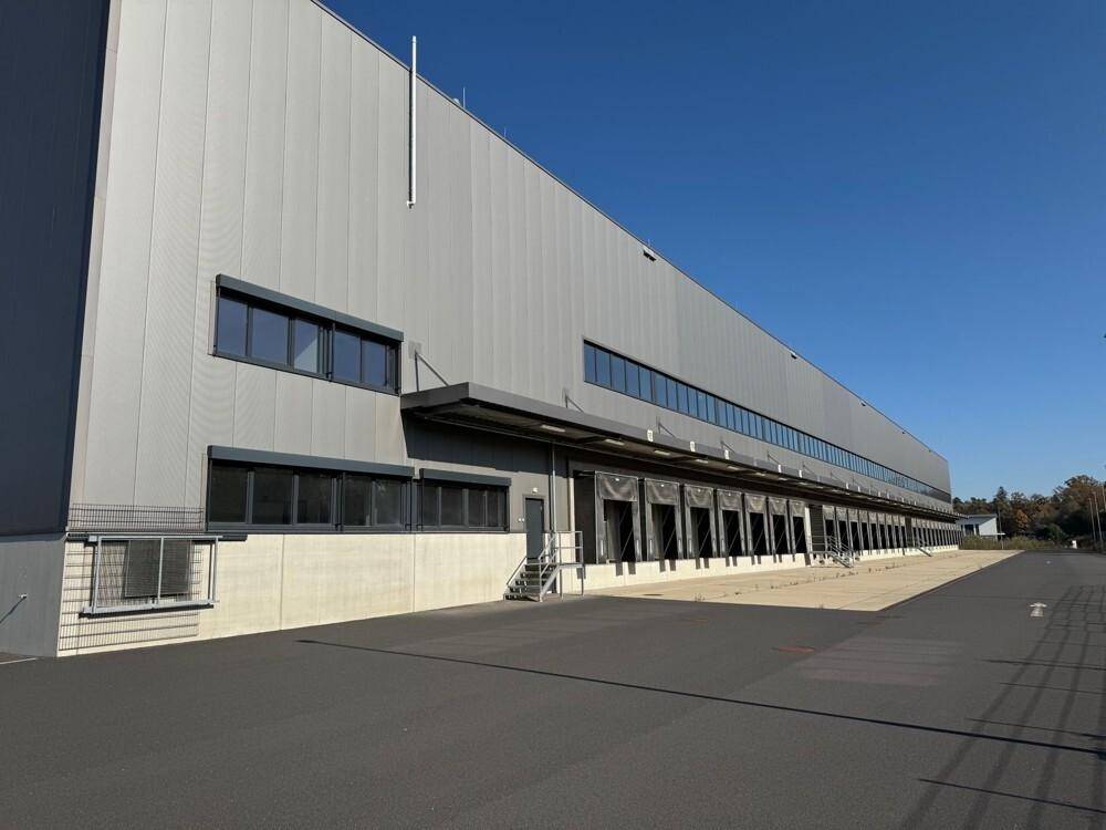 Lange Fassade des Logistikgebäudes mit zahlreichen Laderampen und Fenstern bei Sonnenschein.
