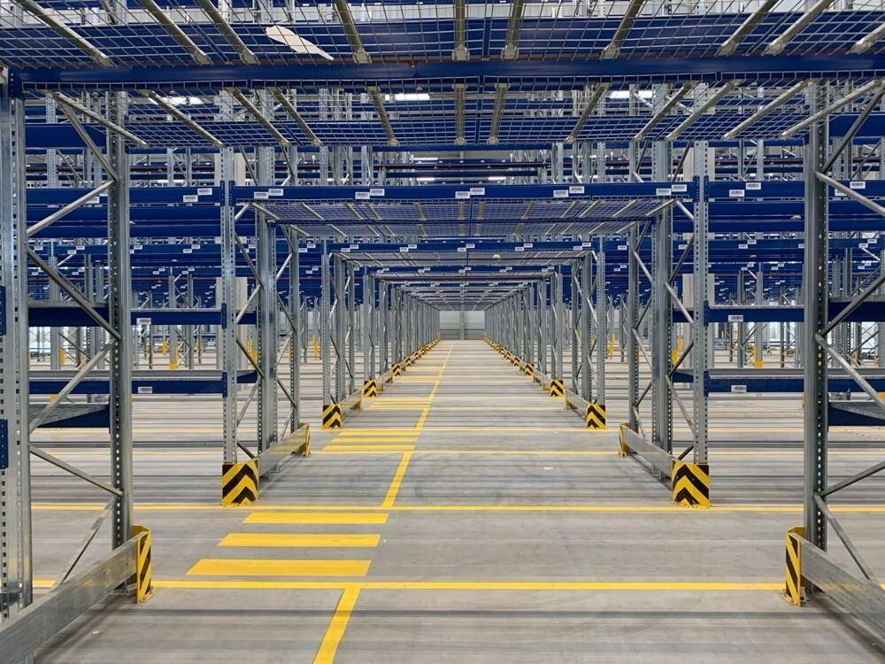 Innenansicht einer modernen Lagerhalle mit hohen Regalsystemen und gelben Bodenmarkierungen.