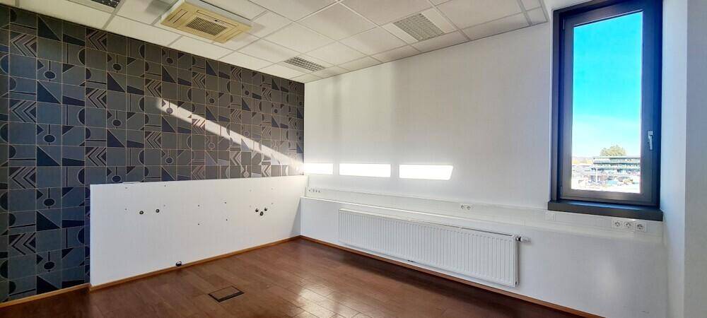 Büro mit dunkler Mustertapete, Holzboden und einem Fenster, das Tageslicht hereinlässt.