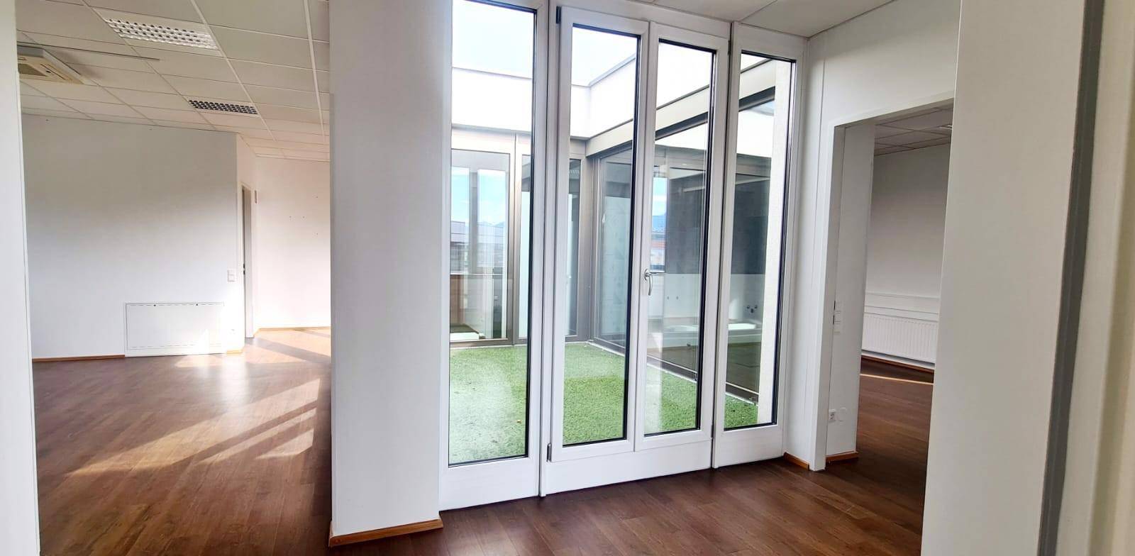 Heller Bürobereich mit Holzboden und einer beeindruckenden Glasfront zum begrünten Atrium.