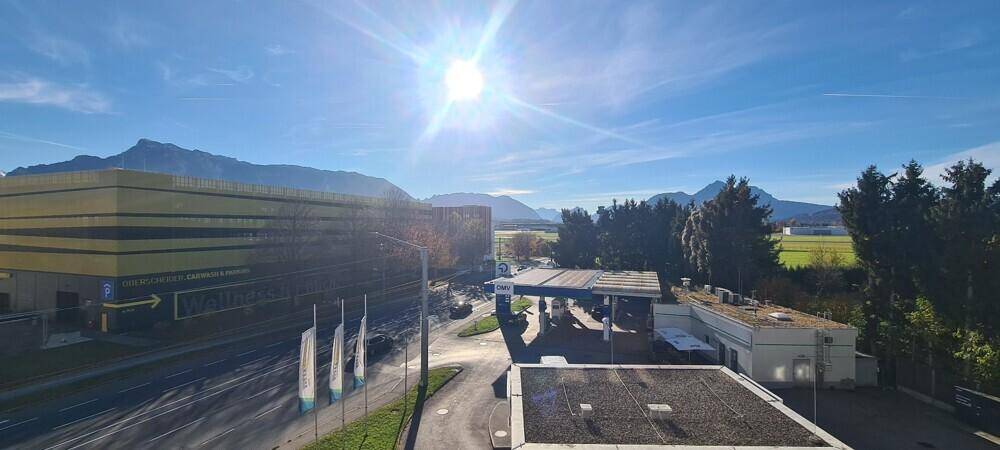 Weitläufiger Ausblick auf die Umgebung mit Straße, Tankstelle, Gebäuden und Bergen im Hintergrund.