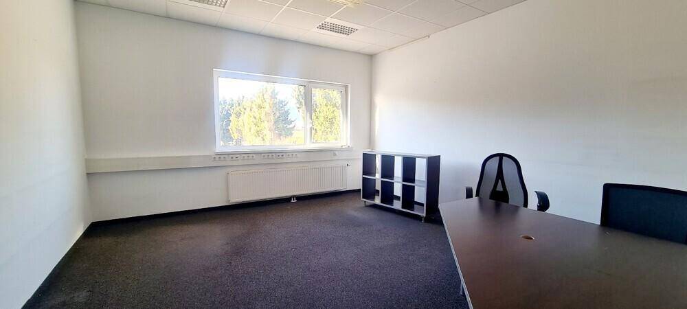 Büroraum mit Schreibtisch, Stuhl und Regal, ausgestattet mit Teppichboden und großem Fenster.