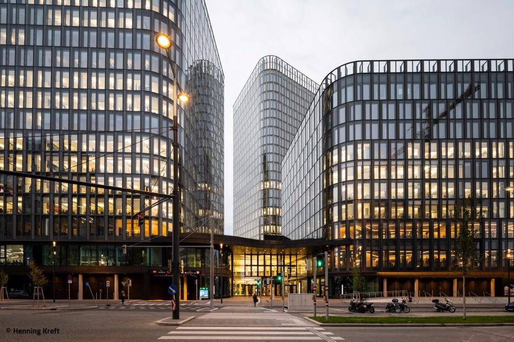 Architektonische Glasgebäude bei Dämmerung, umgeben von einer städtischen Kreuzung mit Lichtern.