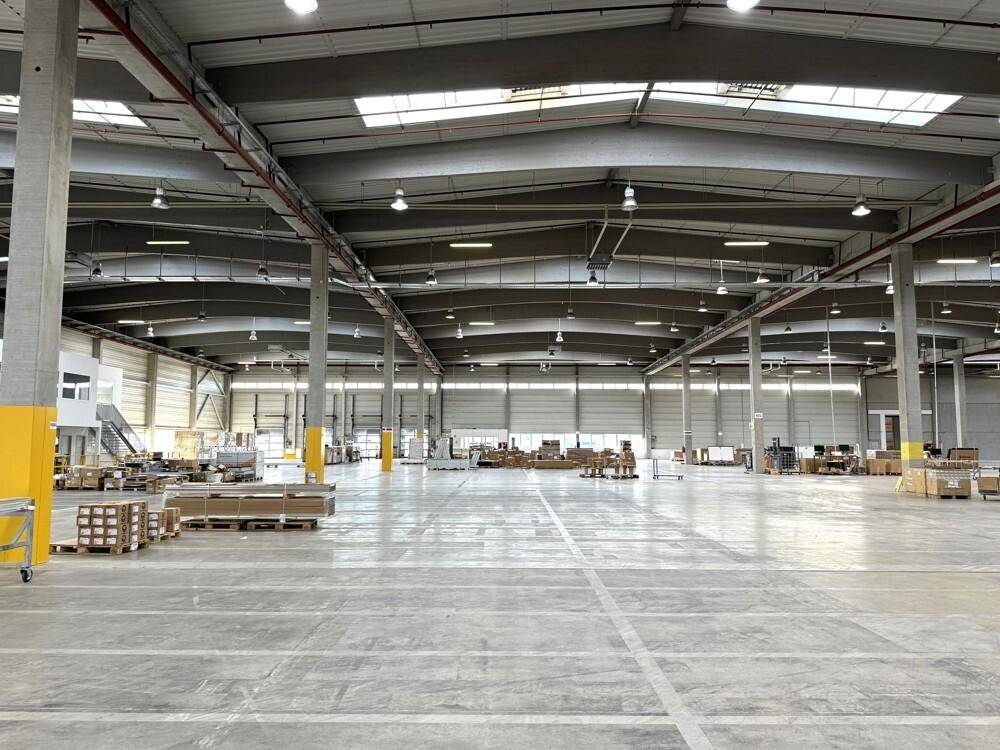 Weitläufige Lagerhalle mit hohen Decken, Betonboden und einigen palettierten Waren.
