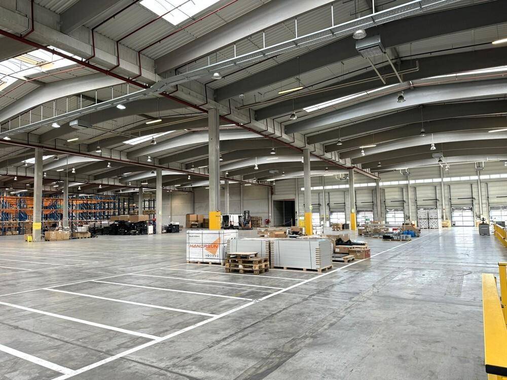 Geräumige Lagerhalle mit Betonboden, hohen Decken und sichtbaren Laderampen im Hintergrund.