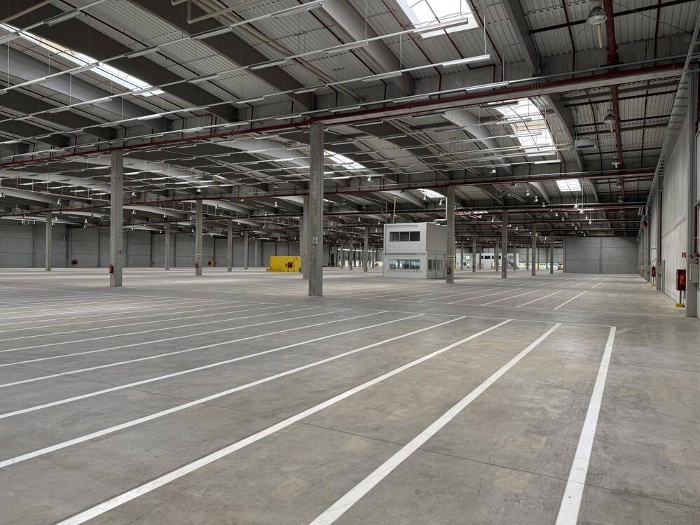 Weitläufige, leere Lagerhalle mit Betonboden, hohen Decken und einem integrierten Bürogebäude.