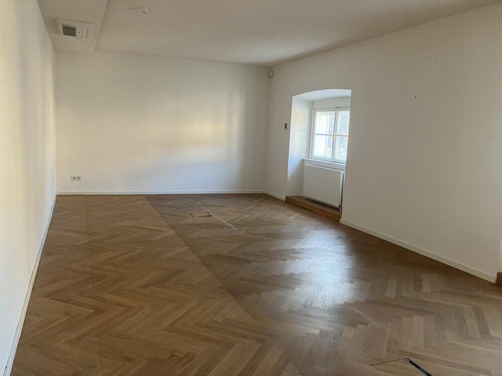 Geräumiger, heller Büroraum mit Fischgrätparkett und einem Fenster mit Blick nach draußen.