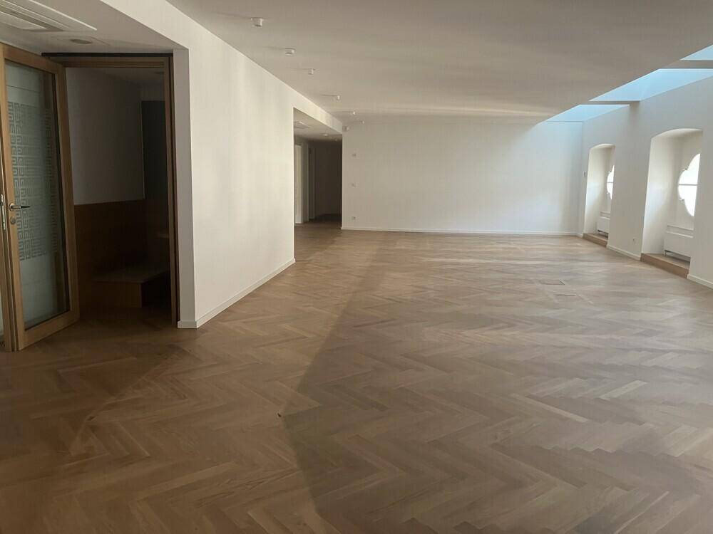 Geräumiger, heller Büroraum mit elegantem Fischgrätparkett und hohen Decken.