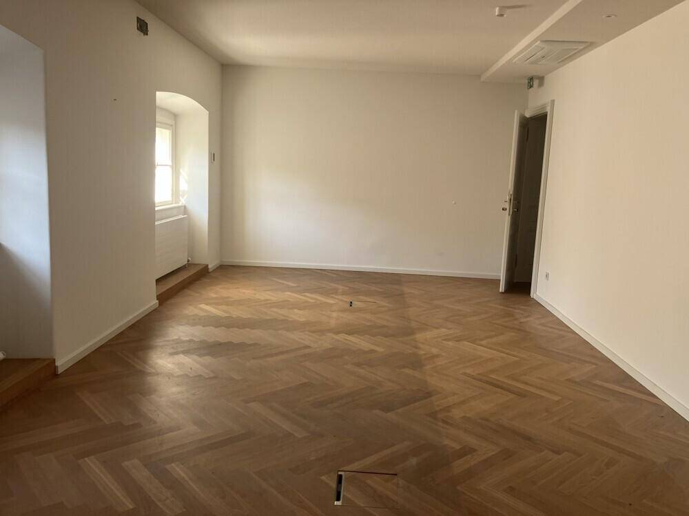 Heller, leerer Büroraum mit Fischgrätparkett und einem Fenster mit tiefer Laibung.