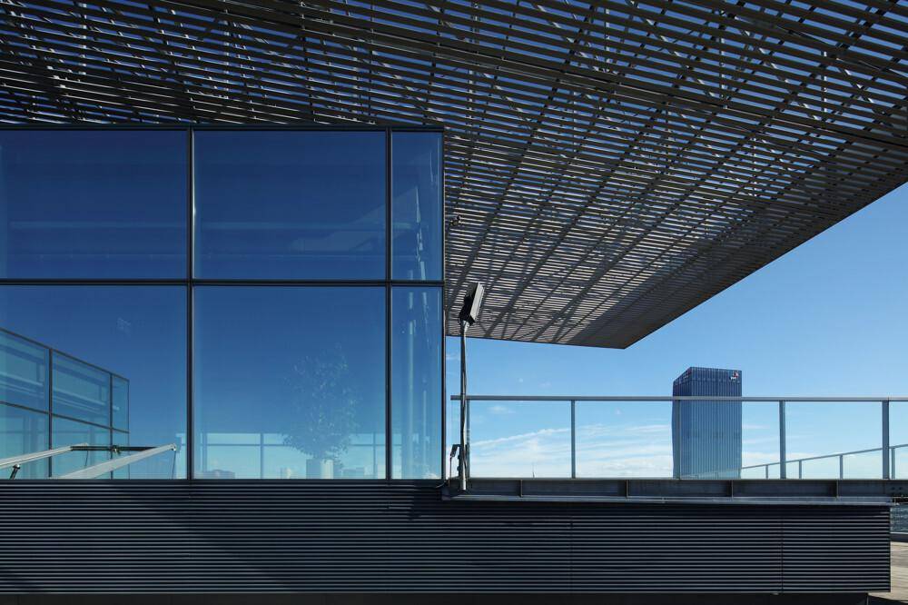 Dachterrasse mit Metallstruktur, Glasgeländer und Blick auf die umliegende Stadtlandschaft.