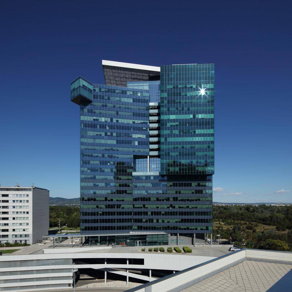 Modernes Bürogebäude mit blauer Glasfassade unter klarem Himmel und umliegender Landschaft.