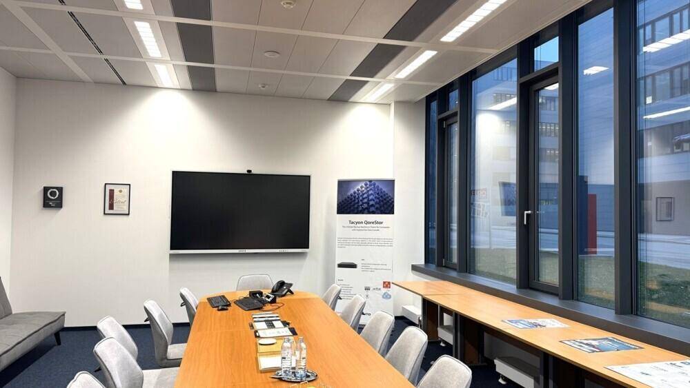 Heller Konferenzraum mit großem Holztisch, bequemen Stühlen und einem Wandbildschirm für Präsentationen.