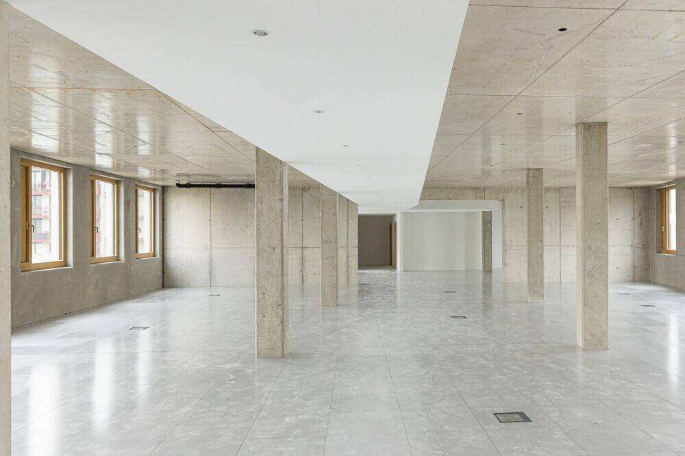 Großer, offener Rohbau mit Betonstützen, Fliesenboden und vielen Fenstern für natürliches Licht.