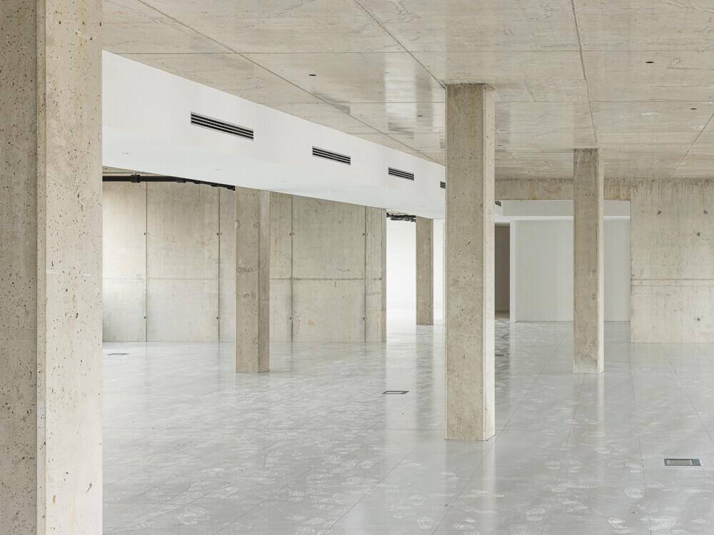 Großer, offener Rohbau mit vielen Betonstützen, Fliesenboden und Belüftungsschlitzen an der Decke.