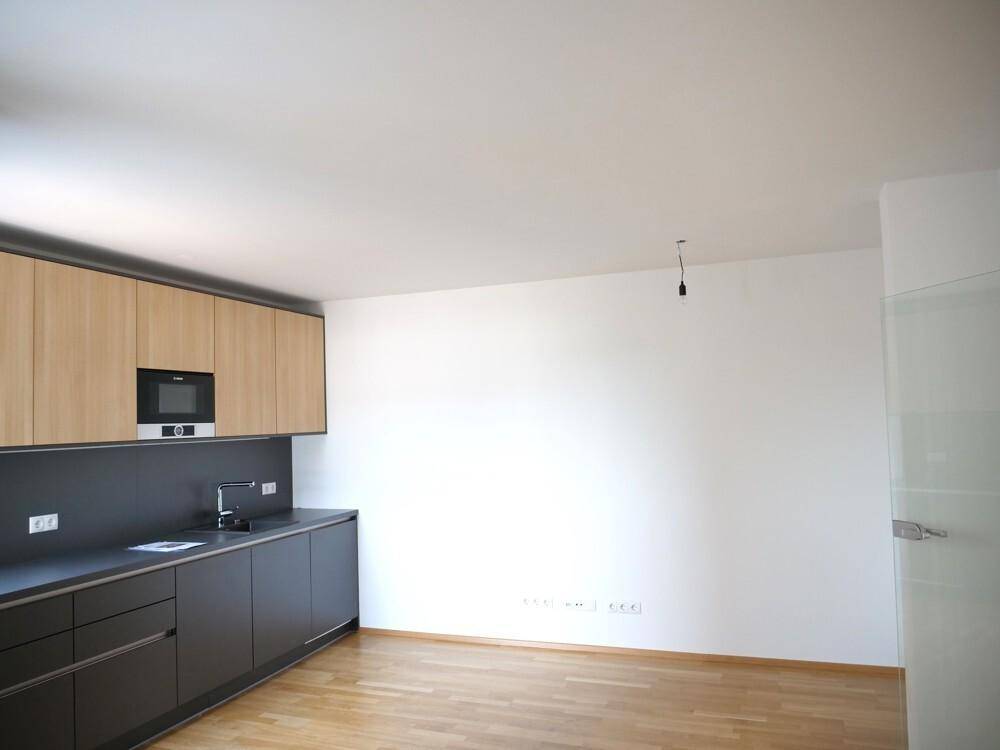 Moderne Einbauküche mit dunklen Unterschränken und hellen Holz-Oberschränken in einem leeren Raum.