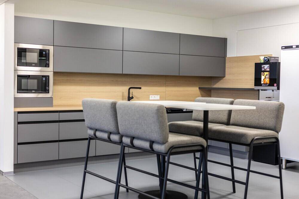 Moderne Büroküche mit grauen Schränken, Holzakzenten und integrierten Mikrowellen, ideal für Pausen.