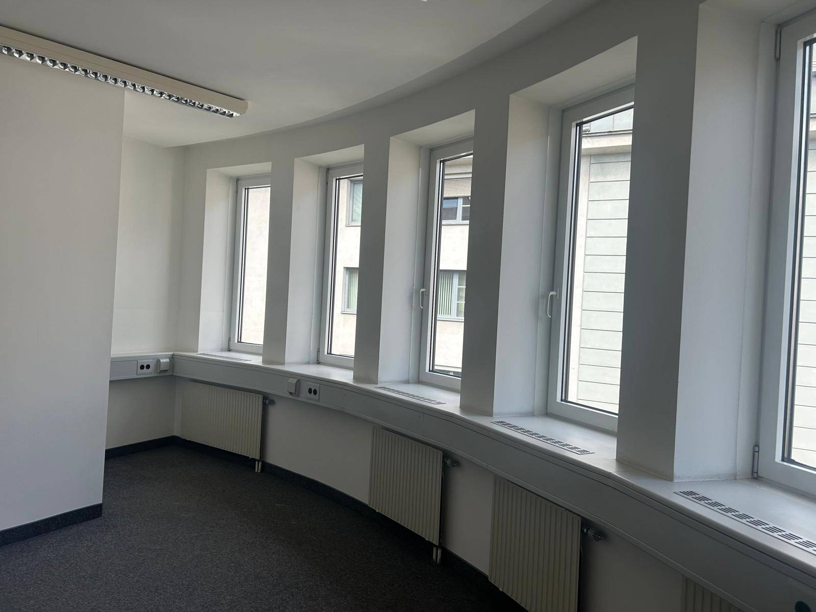 Helles Büro mit Teppichboden und einer Reihe von Fenstern entlang einer geschwungenen Wand, die viel Licht hereinlassen.