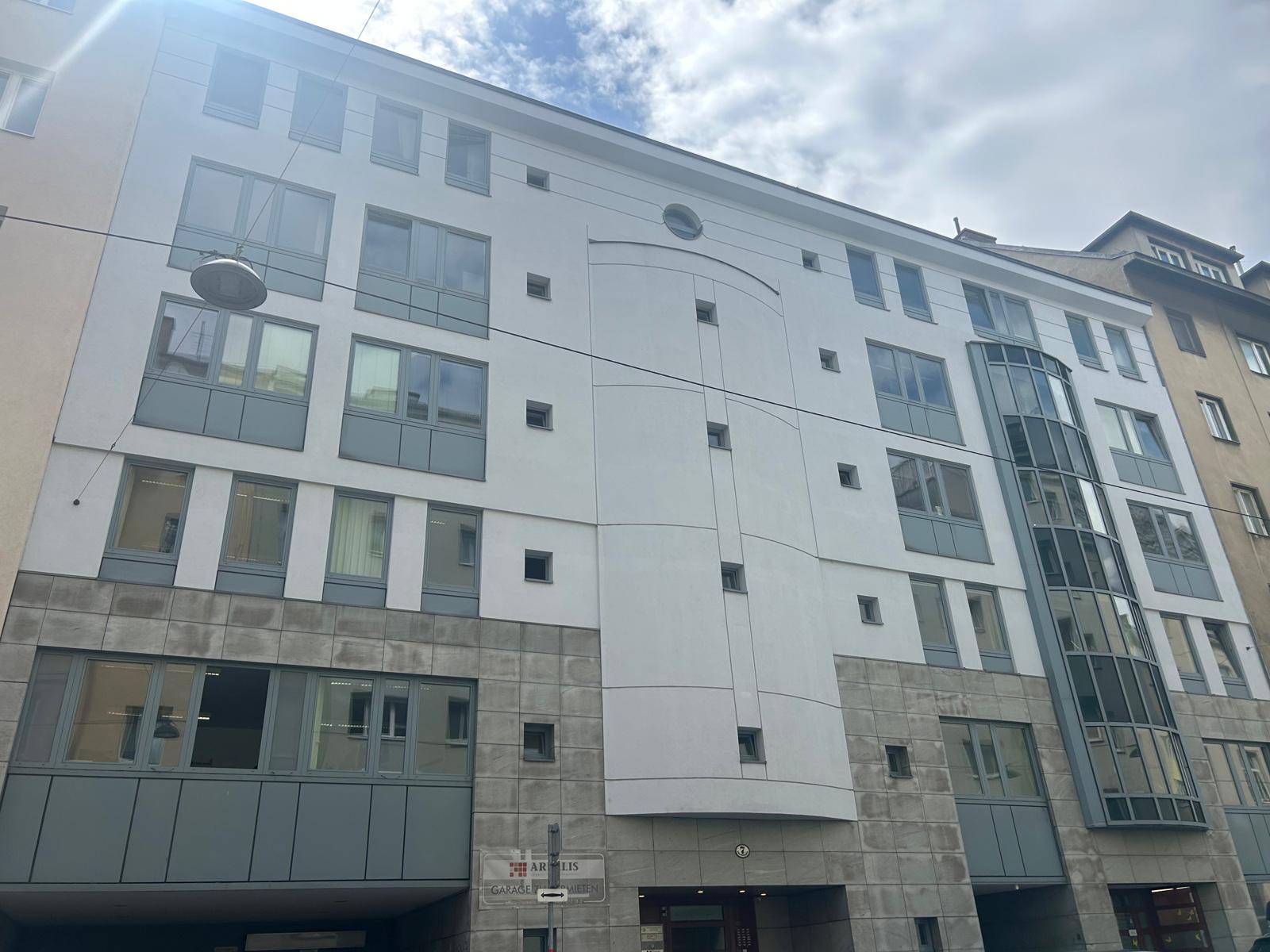 Moderne Gebäudefassade mit weißer und grauer Verkleidung, großen Fenstern und einem markanten Eingangsbereich.