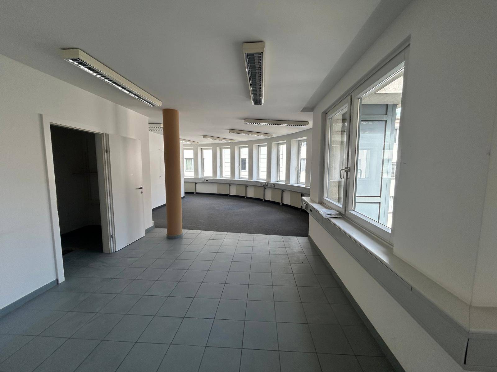 Großes, offenes Büro mit Fliesen- und Teppichboden, vielen Fenstern und viel Tageslicht.