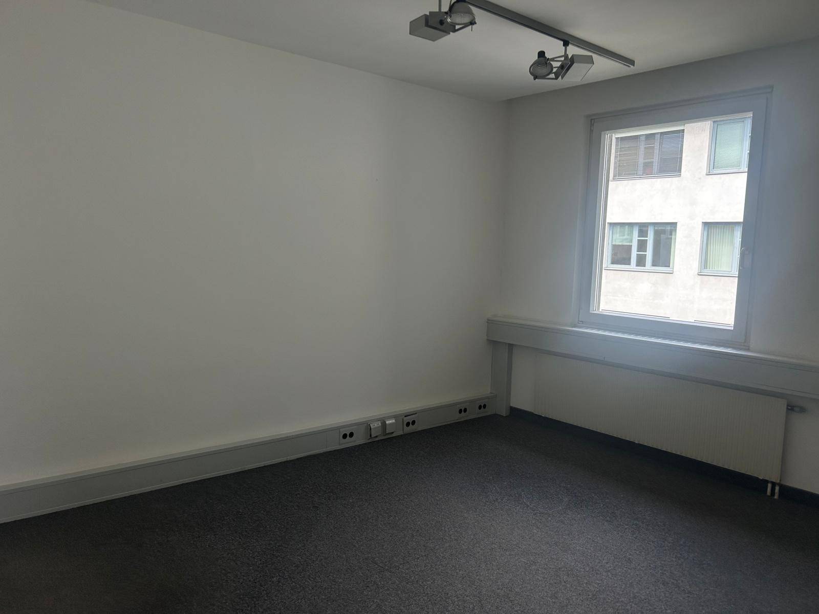 Leeres Büro mit Teppichboden, einem Fenster und Wandanschlüssen, bereit zur individuellen Gestaltung.