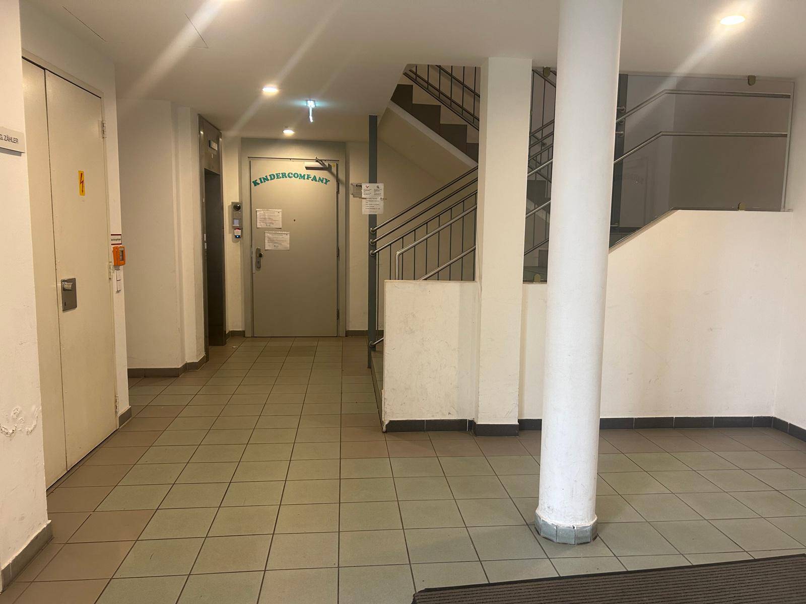 Geräumiger Eingangsbereich mit Fliesenboden, Treppenaufgang und Zugang zu einem Aufzug.